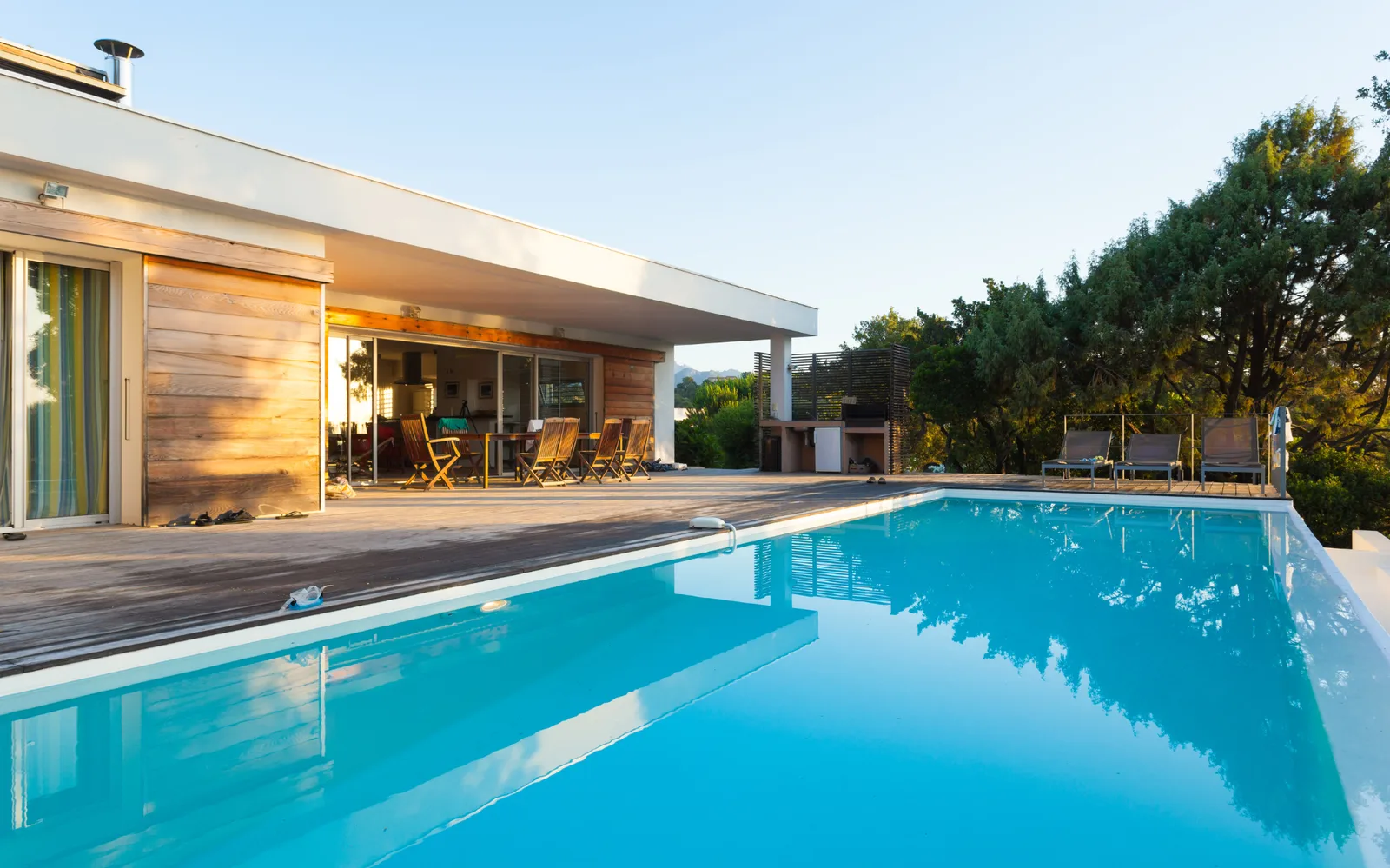 Piscine bordée d'une terrasse en bois devant une maison basse